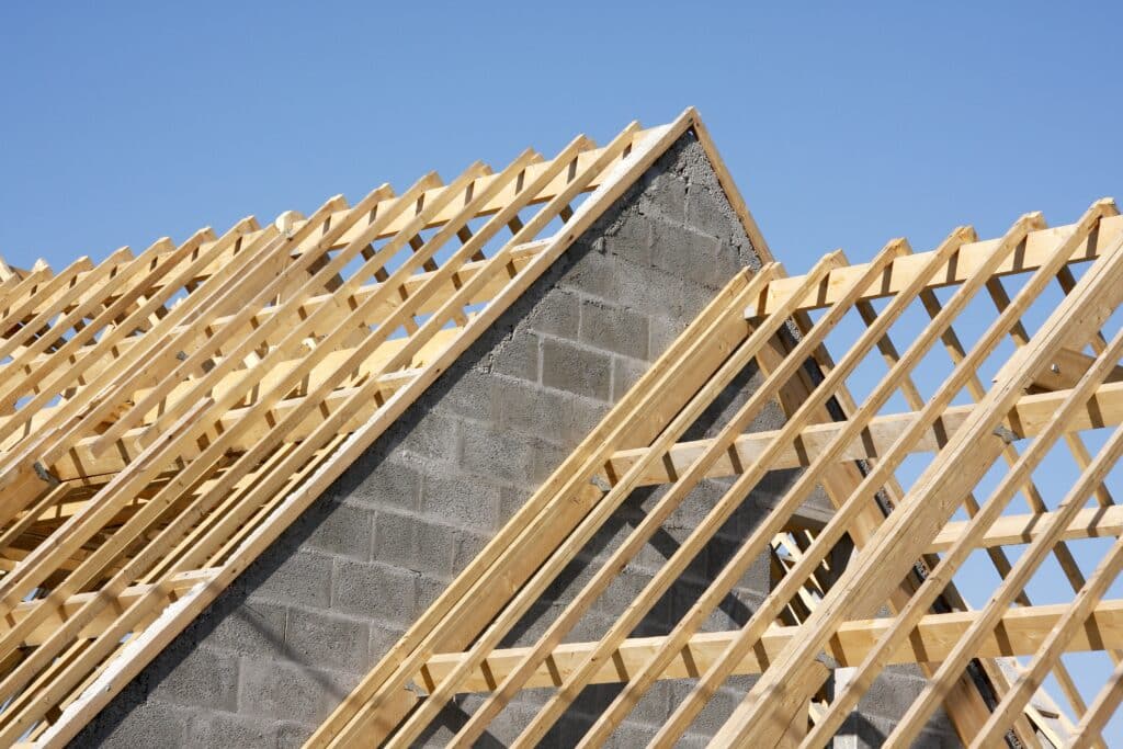 Charpente Bois Neuve sur Maison en Construction Charpente en bois neuve installée sur un pignon en parpaings gris sous un ciel bleu clair, illustrant une construction de toit.